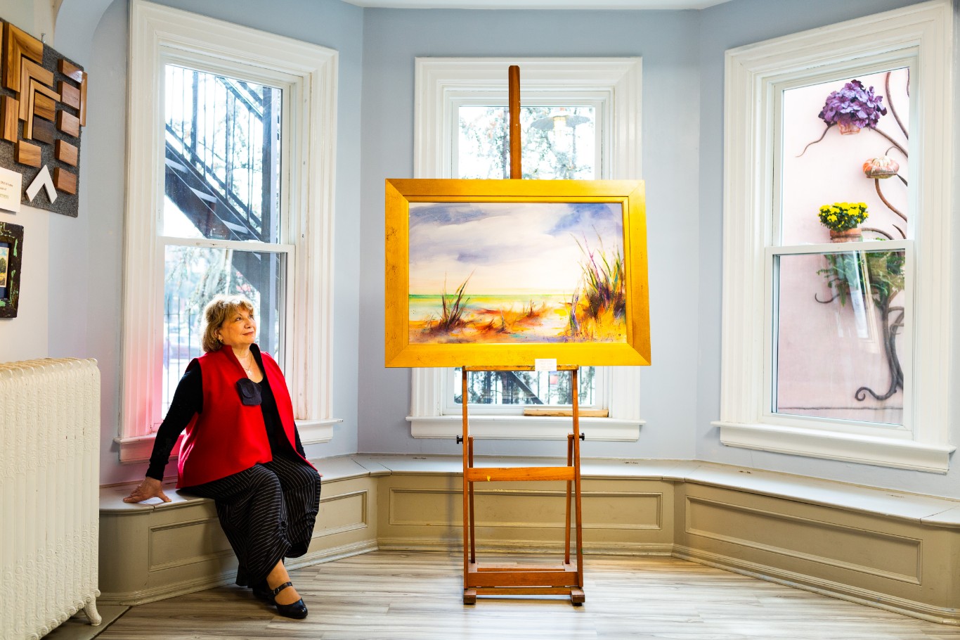 A senior woman sitting on a bench in front of a painting in a continuing care community.