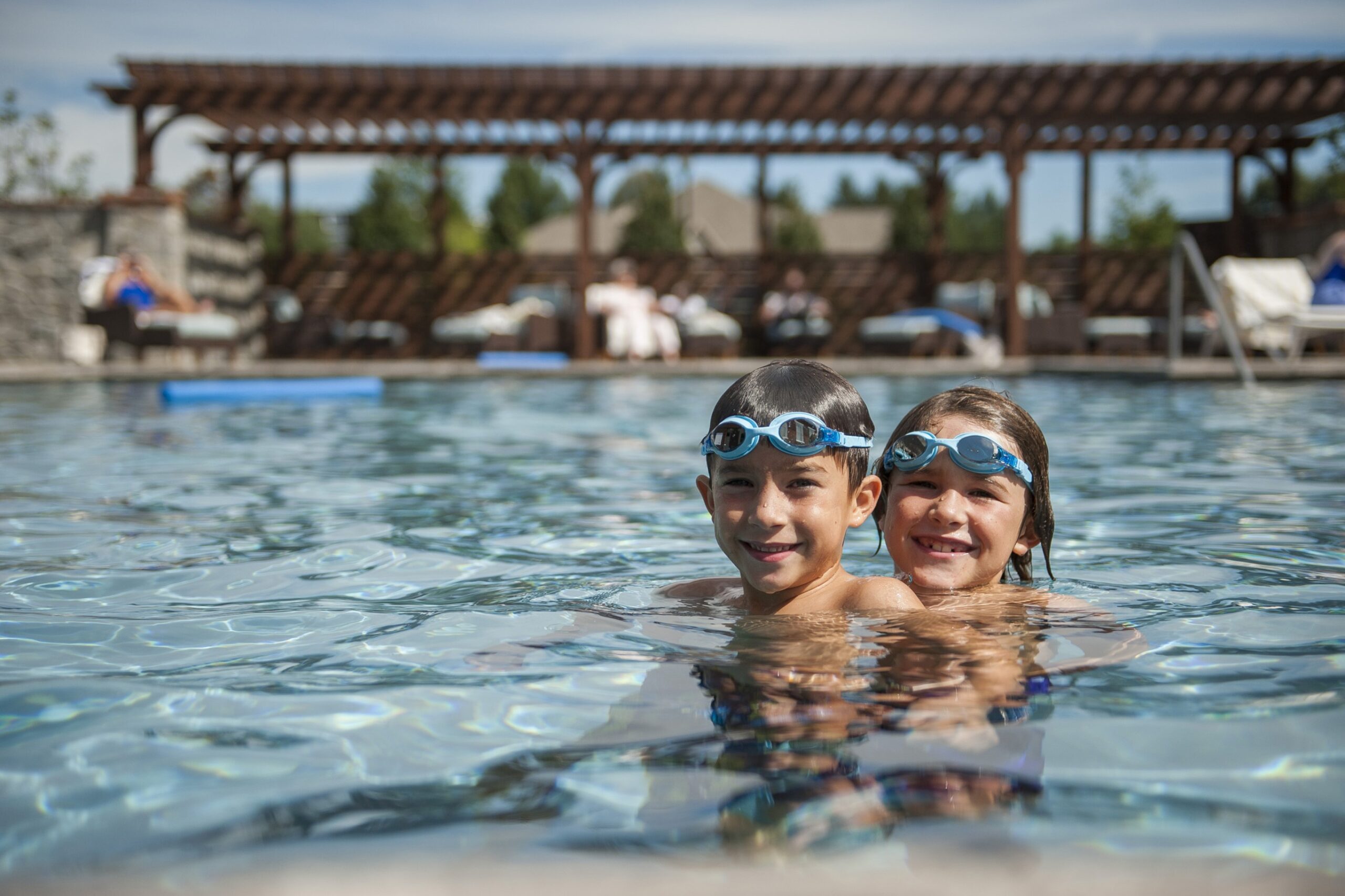 Two children wearing goggles in a swimming pool, enjoying the independence of swimming independently in a senior living community.