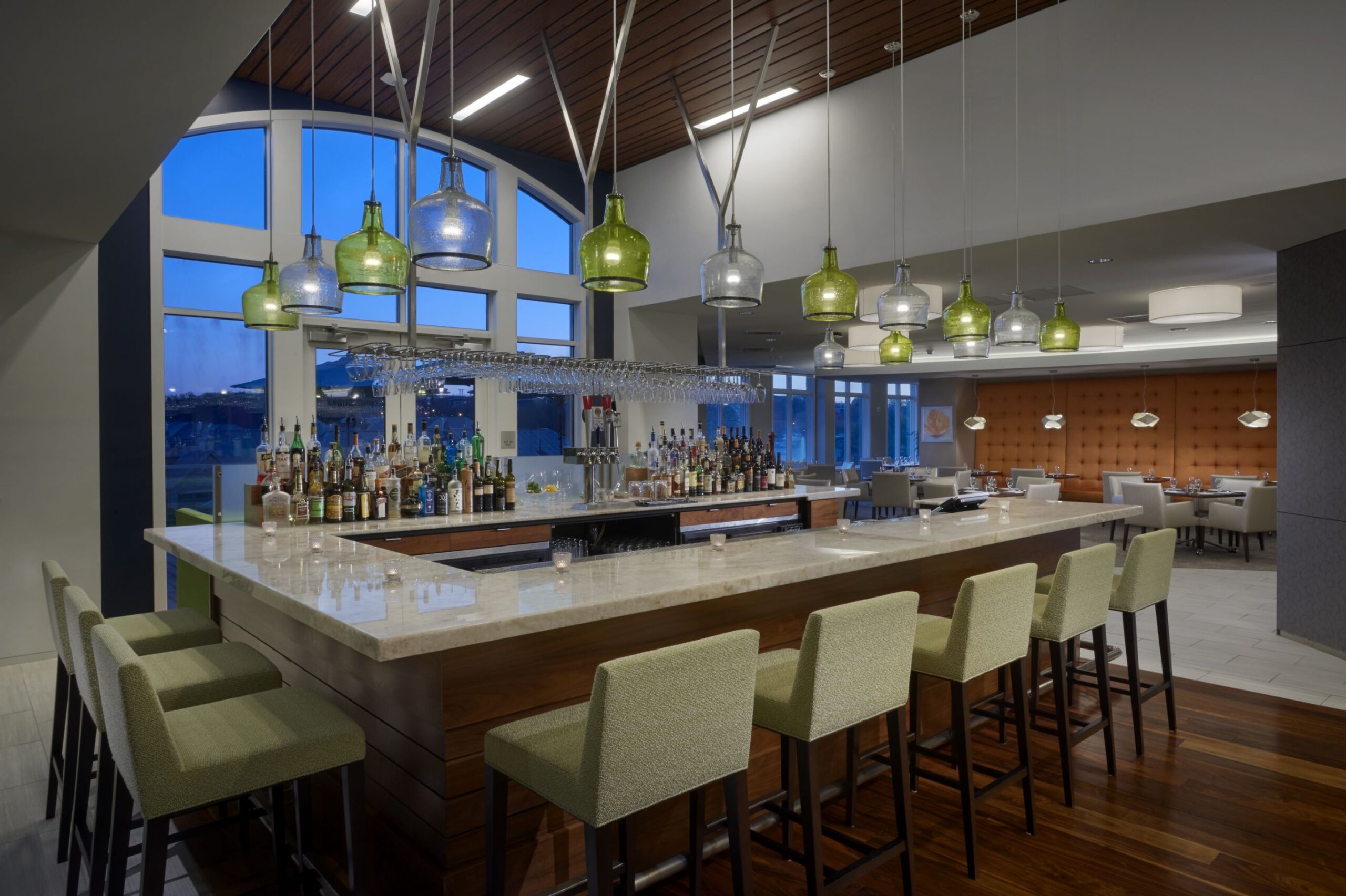 A retirement community with a bar featuring stools and wine bottles hanging from the ceiling.