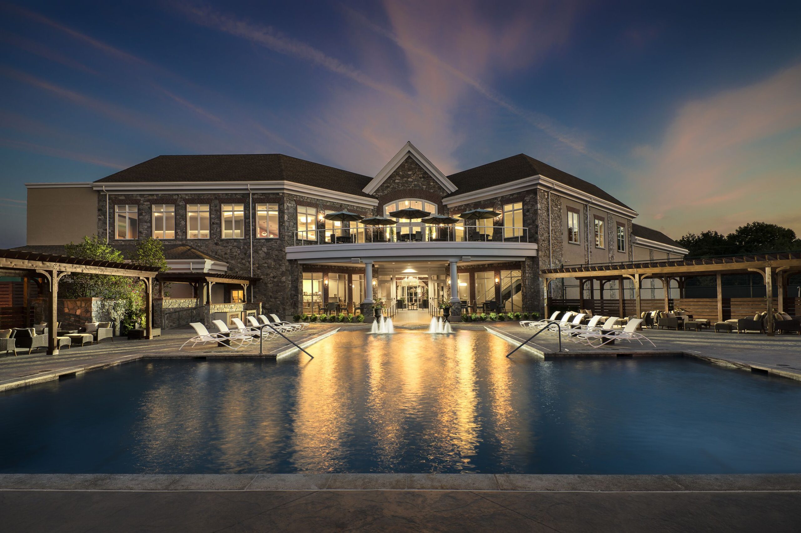 An upscale retirement community featuring a grand mansion set amidst lush surroundings, including a sparkling swimming pool, with a breathtaking dusk view.