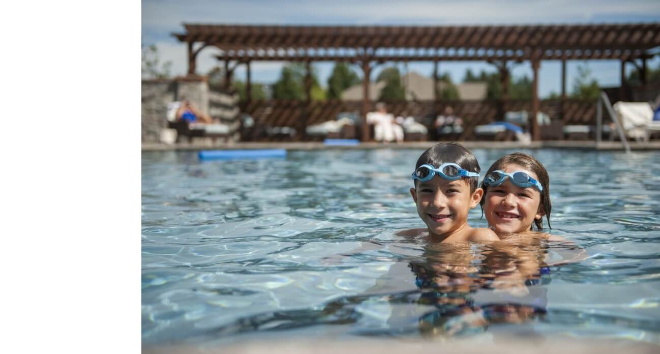 Two children wearing goggles enjoy a swim in the retirement community swimming pool.