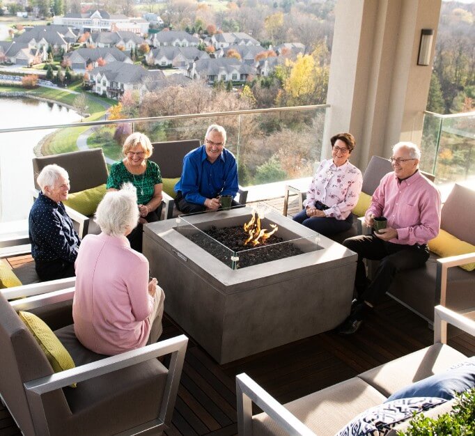 A group of 55+ seniors enjoying independent living gather around a fire pit on a rooftop.