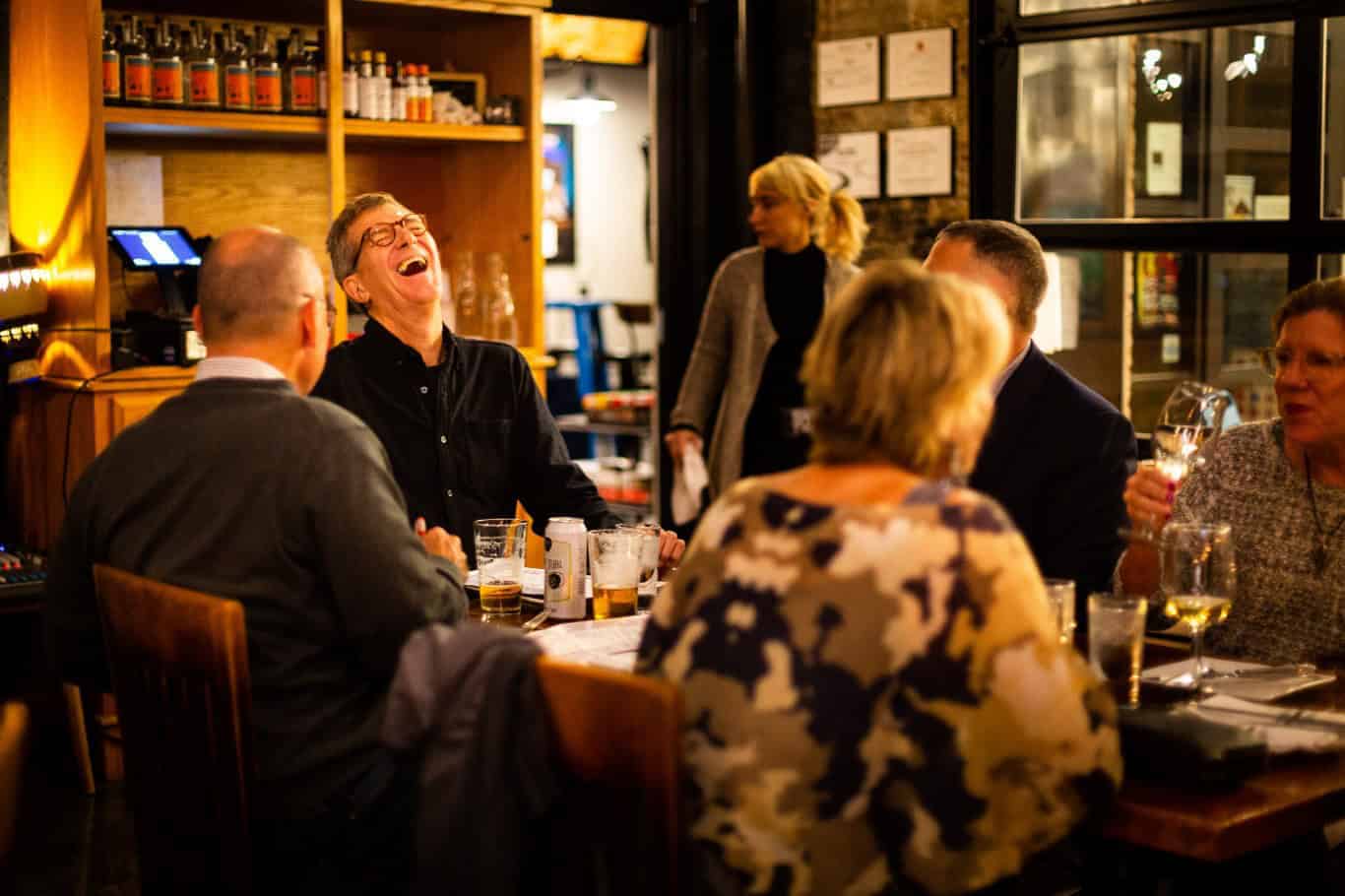 A group of 55+ individuals in a senior living community laughing at a table in a restaurant.